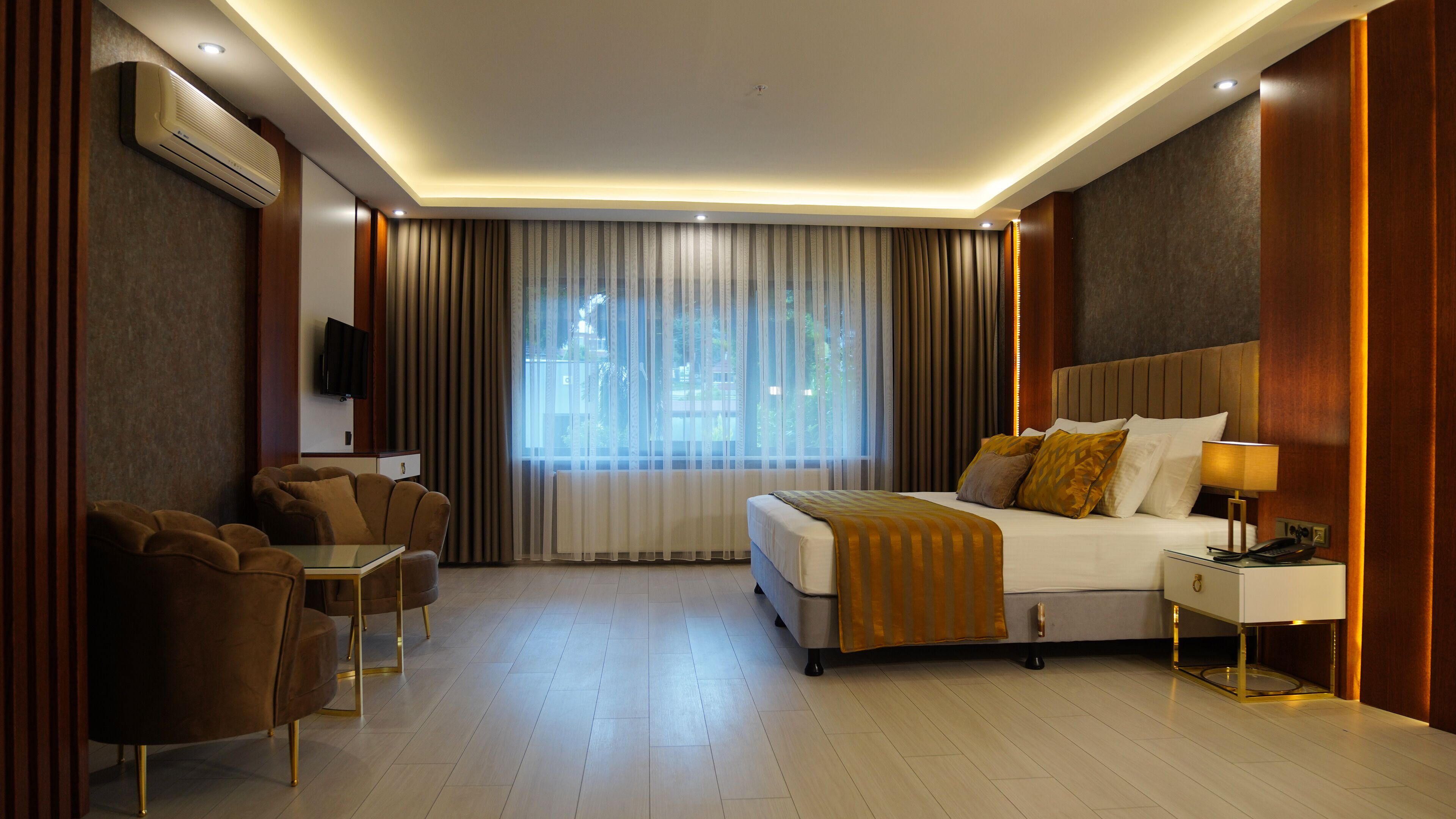 Ein modernes Hotelzimmer mit einem großen Bett, einem Schreibtisch mit Lampe, einem Fernseher und einer Sitzecke mit Sesseln.