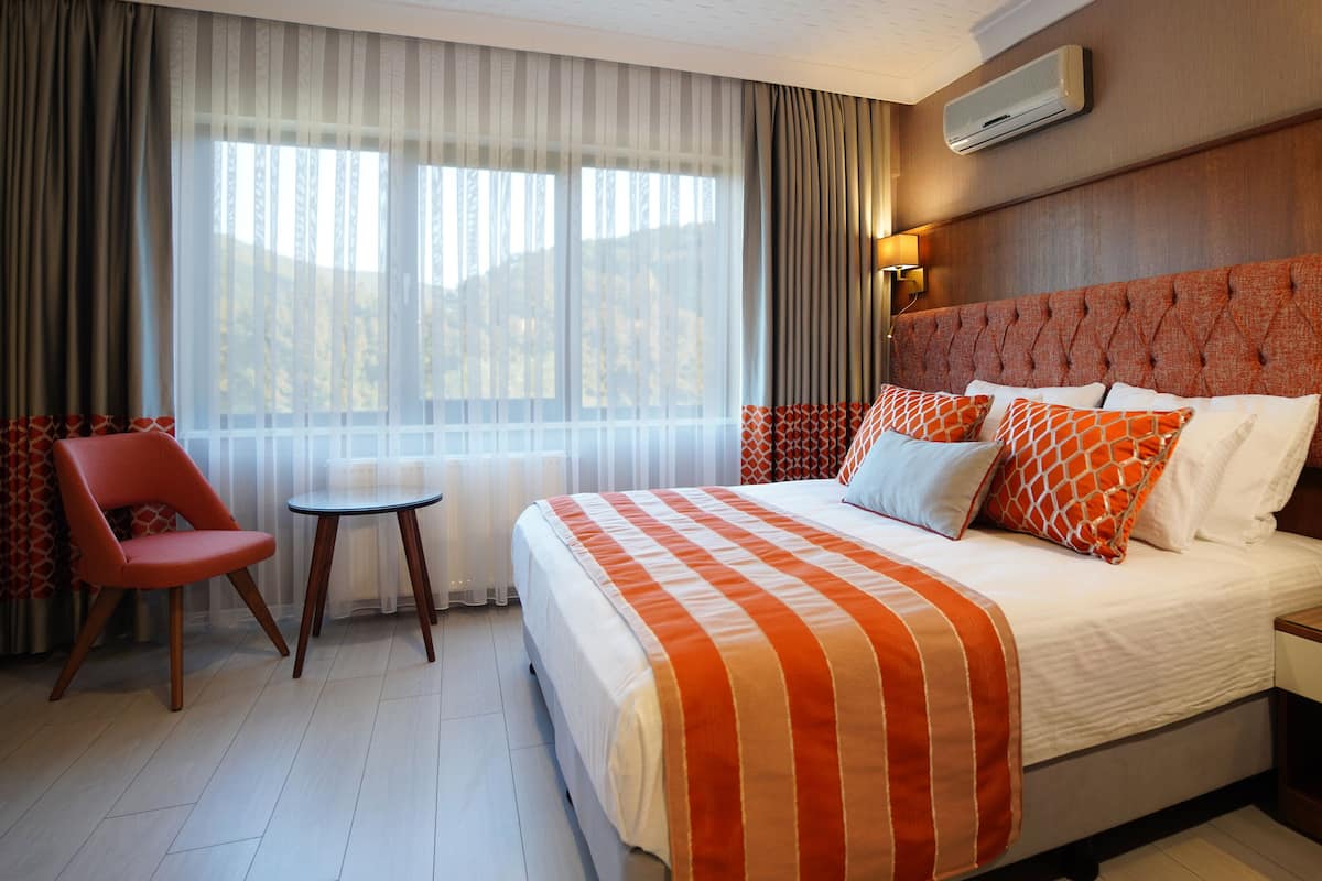 Ett hotellrum med en stor säng, en stol, ett litet bord och en telefon vid sängen.