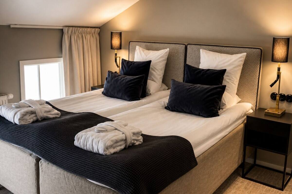 A modern hotel room with a large bed, two bedside tables, and a window with curtains.