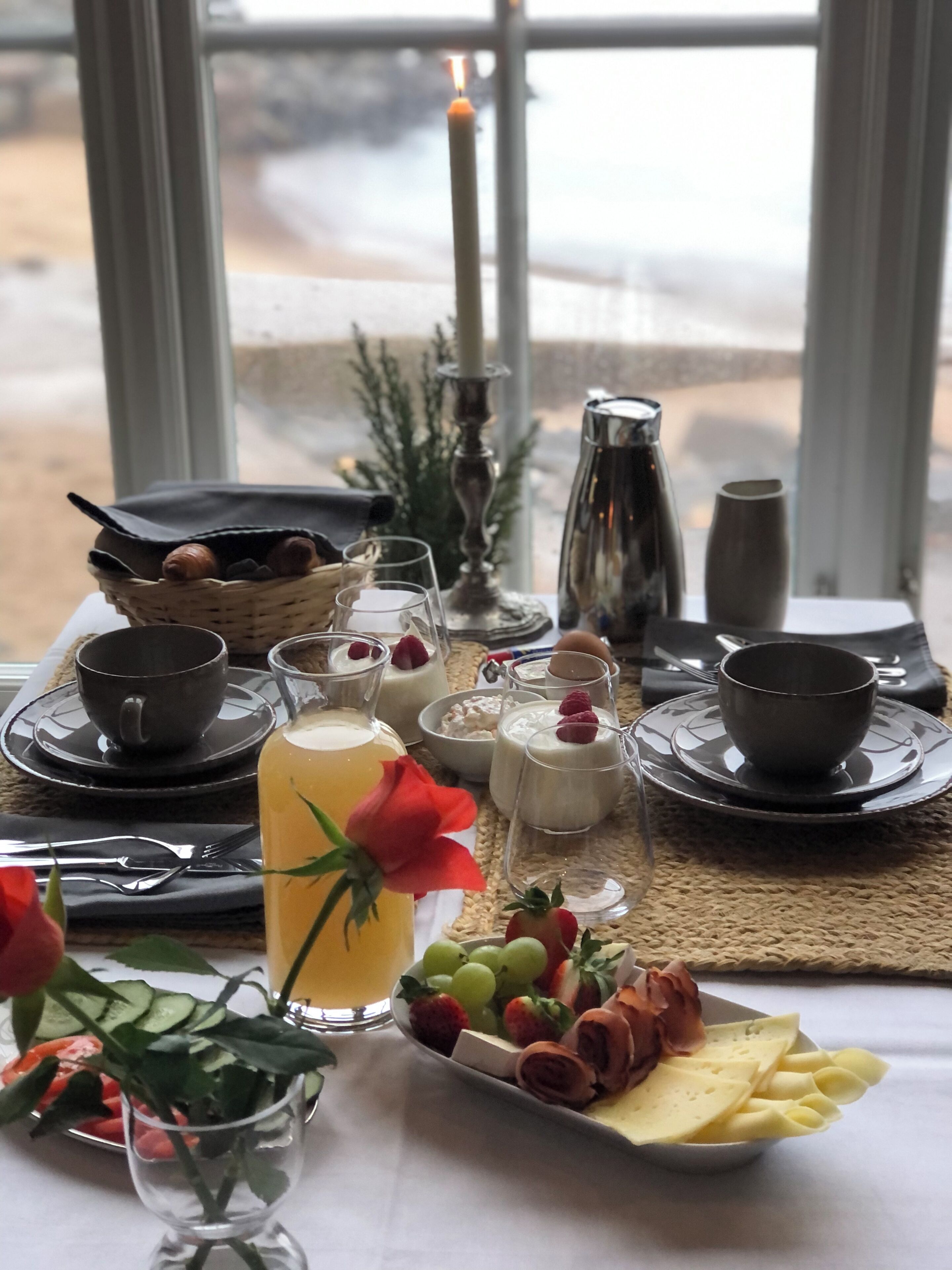 A breakfast setting with a table set for two, featuring a variety of food and drink items, including a fruit platter, cheese, and a glass of orange juice.