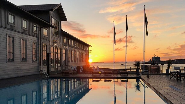 A poolside view with a sunset, a building with large windows, and flags. - Marstrands Kurhotell  (Marstrand)