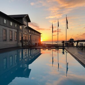 Vista de la piscina con un atardecer, un edificio con amplias ventanas y banderas.