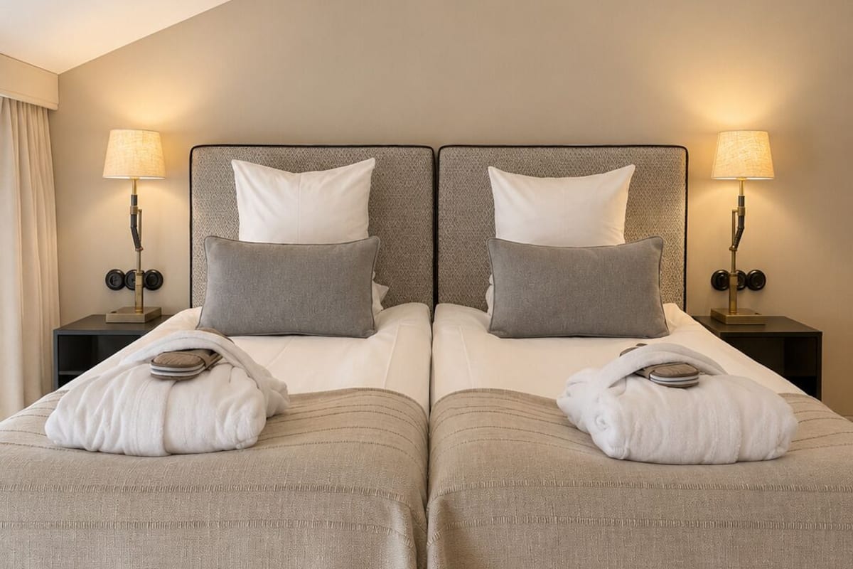 A double bed with two pillows, a bedside table with a lamp, and a window with curtains.
