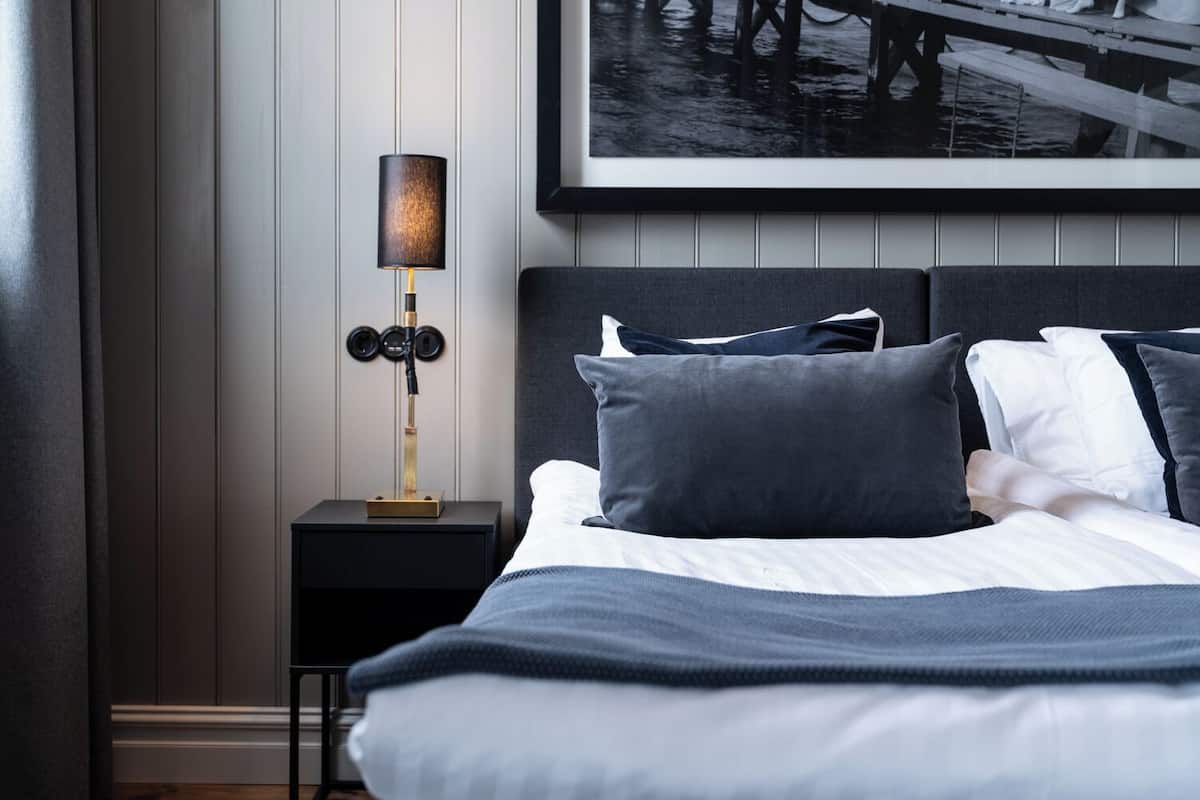 A neatly made bed with a grey and white color scheme, a modern bedside lamp, and a framed picture above the bed.