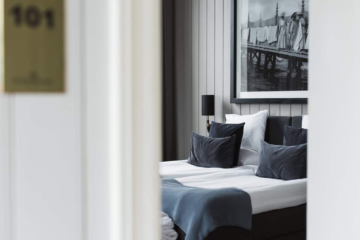 A hotel room with a bed, pillows, a nightstand, a lamp, and a framed picture on the wall.