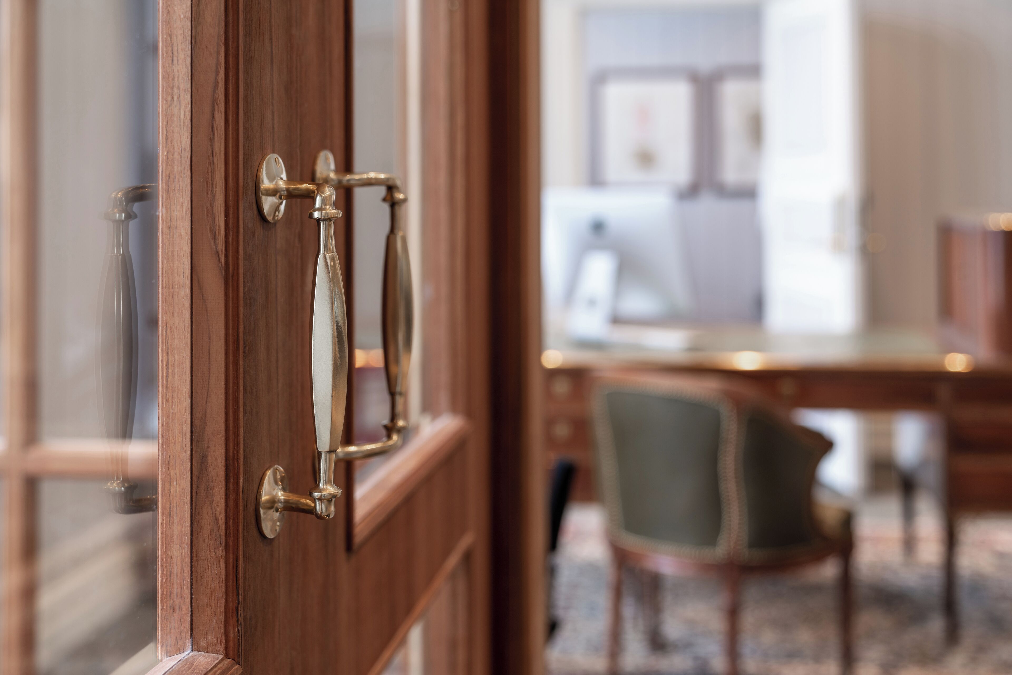 A wooden door with a brass handle, leading to a room with a desk and a chair.