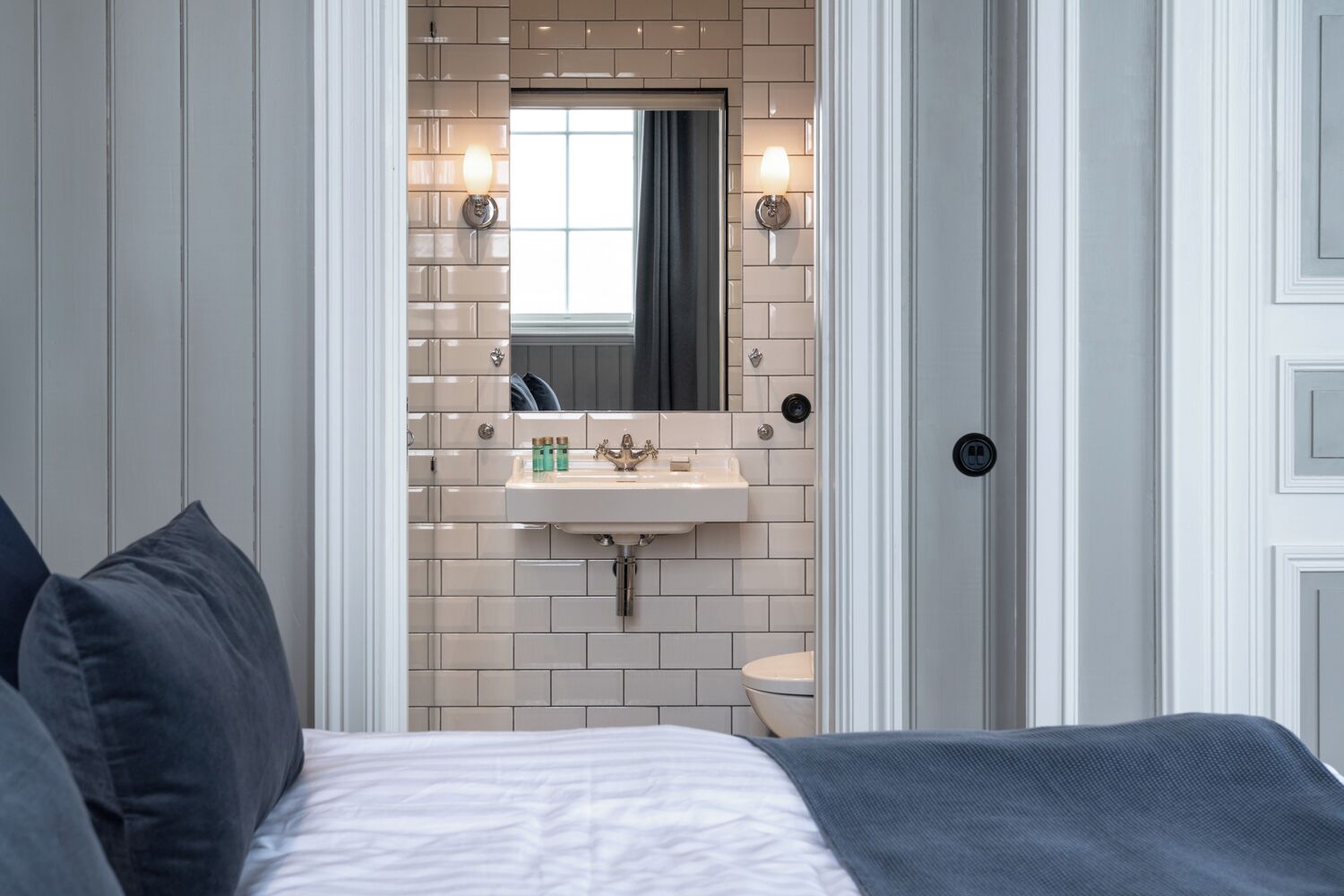 Un dormitorio con cama, mesita de noche, espejo, lavabo e inodoro.