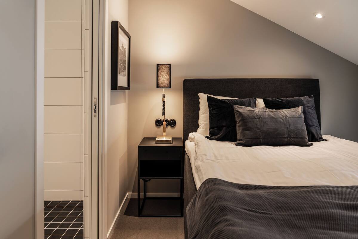A neatly arranged bedroom with a bed, bedside table, lamp, and a framed picture on the wall.