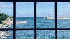 A coastal view through a window with a clear sky, calm sea, rocky shoreline, and a distant lighthouse. - Marstrands Kurhotell  (Marstrand)