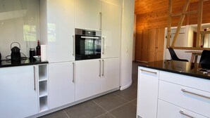 Une cuisine moderne avec des meubles blancs, un réfrigérateur noir et un plafond en bois.