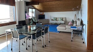 Un amplio salón con techo de madera, una mesa de vidrio para comer con sillas, un sofá y una mesa de centro.