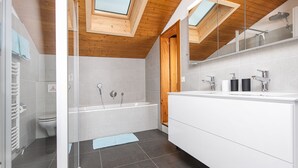 Une salle de bain moderne dotée d’un puits de lumière, d’une baignoire, d’un grand meuble-lavabo et de toilettes.
