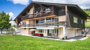 Una casa de dos pisos con un balcón, un patio con mobiliario exterior y un césped bien cuidado.