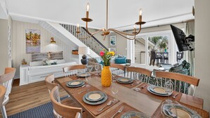 A dining area with a wooden table set for four, a yellow vase with flowers, and a staircase in the background. - OCEANFRONT Views, Community Pool, Modern, Ideal Wild Dunes Location! (Isle Of Palms)
