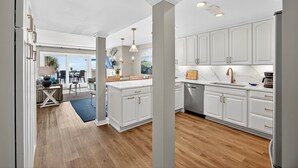 A modern kitchen with white cabinetry, a central island, and a dining area with a view. - OCEANFRONT Views, Community Pool, Modern, Ideal Wild Dunes Location! (Isle Of Palms)