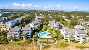An aerial view of a residential area with multiple two-story houses, a central swimming pool, and a clear view of the ocean in the background. - OCEANFRONT Views, Community Pool, Modern, Ideal Wild Dunes Location! (Isle Of Palms)