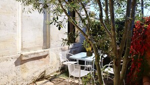 A small outdoor patio with a table and chairs, surrounded by trees and a white wall.