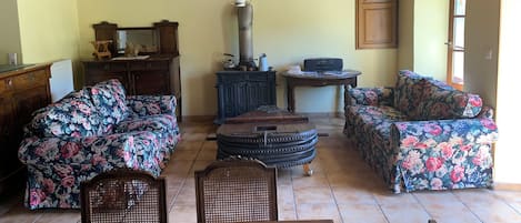 Un salon chaleureux avec des canapés à motifs floraux, une table basse en bois et une radio d’époque.