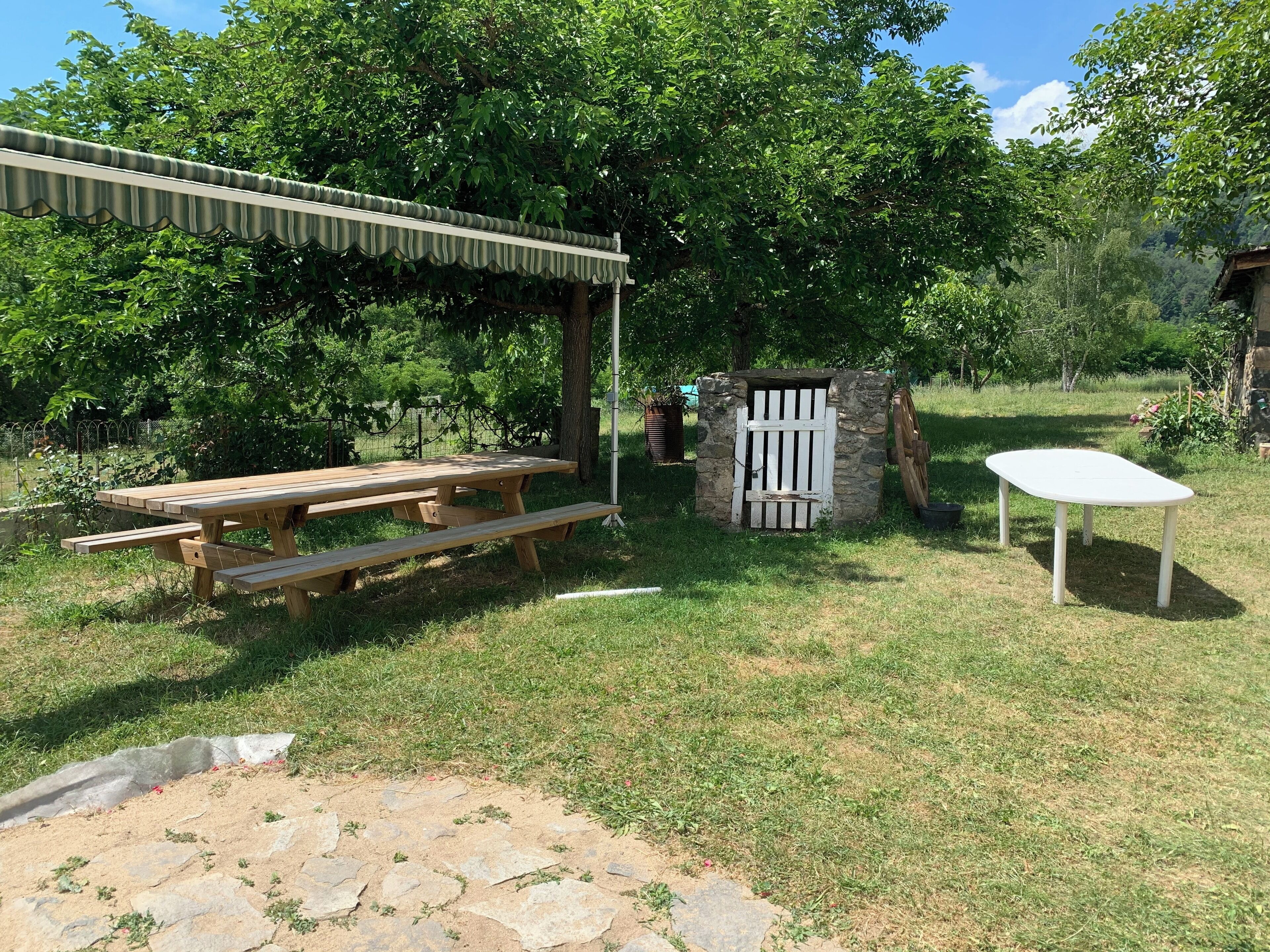 Een houten picknicktafel met bankjes, een stenen constructie met een witte poort, en een klein wit tafeltje.