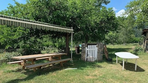 Una mesa de picnic de madera con bancos, una estructura de piedra con un portón blanco y una pequeña mesa blanca.