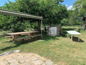 A wooden picnic table with benches, a stone structure with a white gate, and a small white table. - Back in the past (roche en regnier)