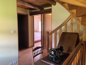 A wooden staircase with a sewing machine on a table, a wooden railing, and a bed in the adjacent room.