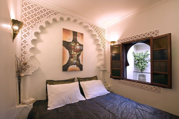 A bedroom with a bed, decorative wall patterns, a window with a view, and a wall-mounted artwork.