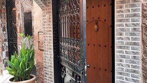 Entrada de un edificio con una puerta numerada, una planta en maceta y pavimento adoquinado.