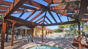 Un espace piscine avec des chaises longues et des parasols sous une pergola en bois.