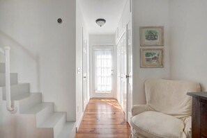 Un pasillo con suelo de madera, paredes blancas y una silla blanca.