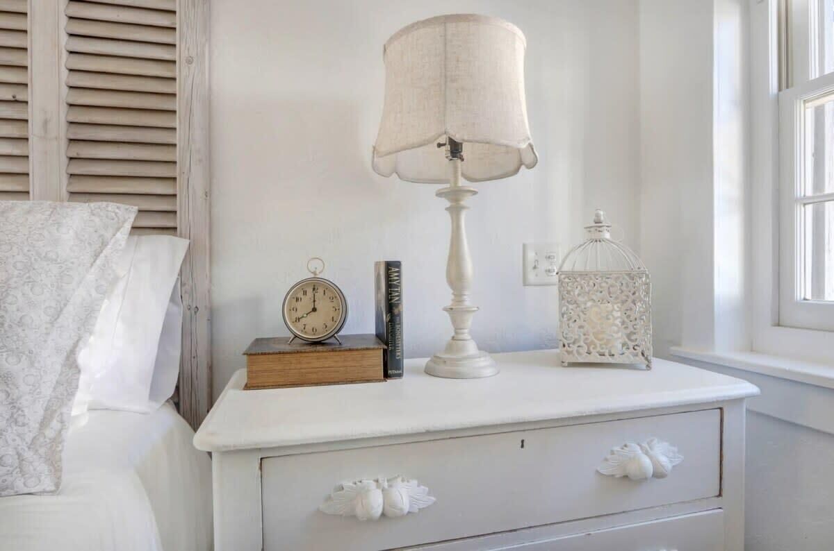 A white bedside table with a lamp, a clock, a book, and a decorative lantern.