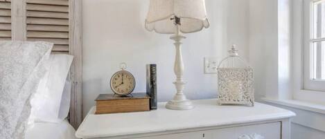 A white bedside table with a lamp, a clock, a book, and a decorative lantern.