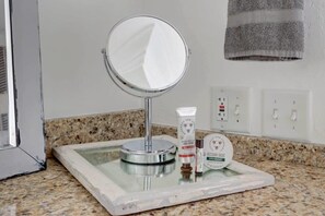 Un meuble-lavabo de salle de bain avec un miroir rond, un distributeur de savon et un petit plateau contenant un flacon de crème pour les mains et un petit récipient à savon rond.