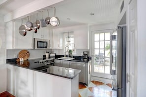 Una cocina moderna con armarios blancos, una isla central, electrodomésticos de acero inoxidable y un amplio ventanal que proporciona luz natural.