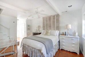 A bedroom with a large bed, a nightstand, a dresser, a ceiling fan, and a staircase.