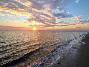 A sunset over a beach with calm waves and a clear sky.