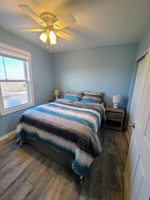A bedroom with a bed, a ceiling fan, a window, and a door.