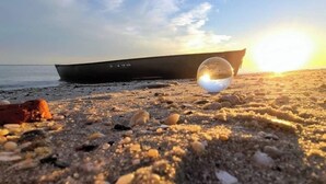En strandscen med en båt och en glaskula som reflekterar solnedgången.