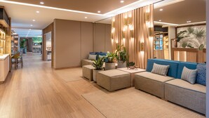 A modern living area with a sofa, ottomans, and a dining area with chairs and a table. - Fairfield by Marriott Medellin Sabaneta (Sabaneta)
