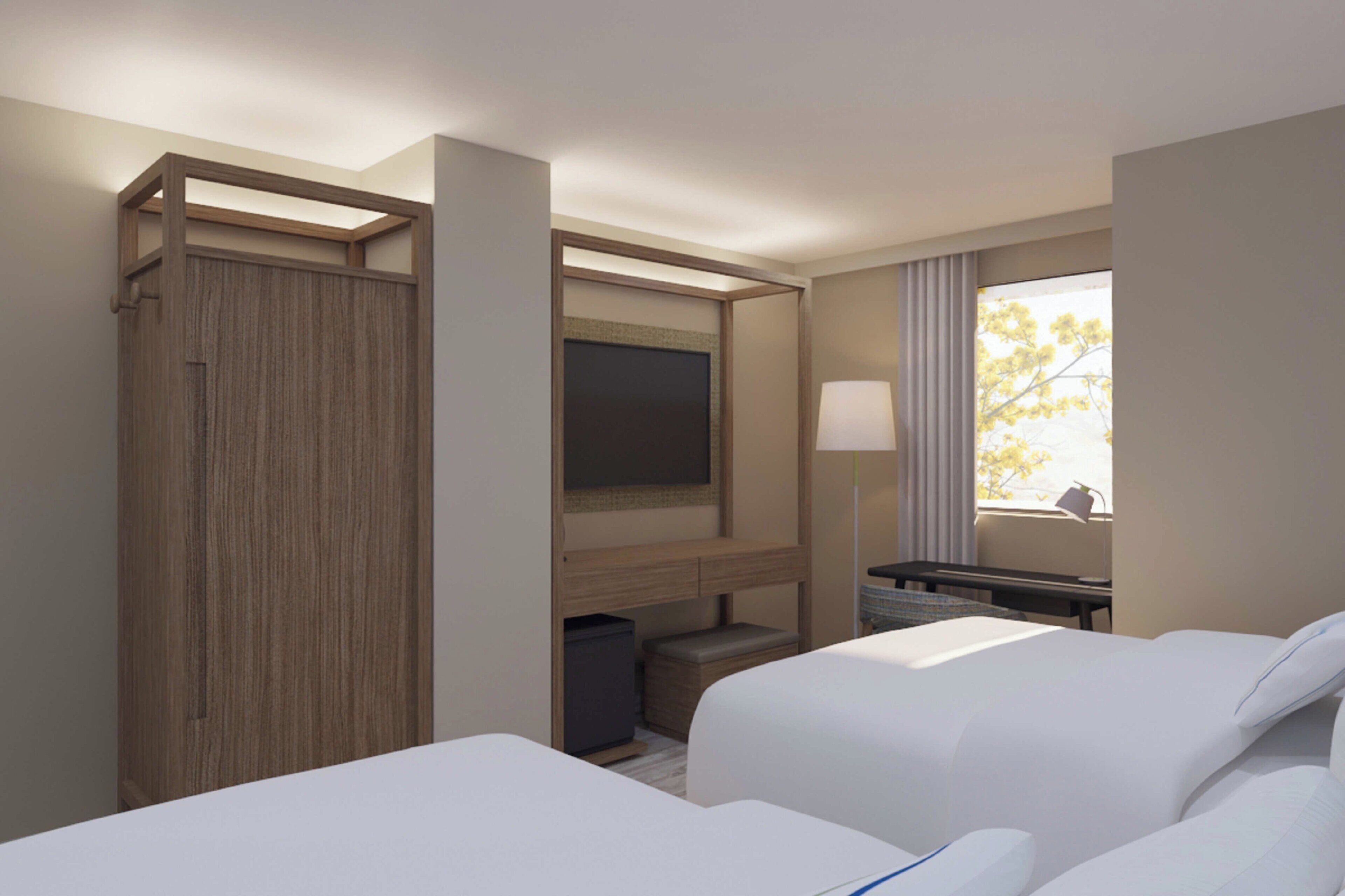 Een hotelkamer met twee bedden, een aan de muur bevestigde televisie, een bureau met lamp en een raam met gordijnen.
