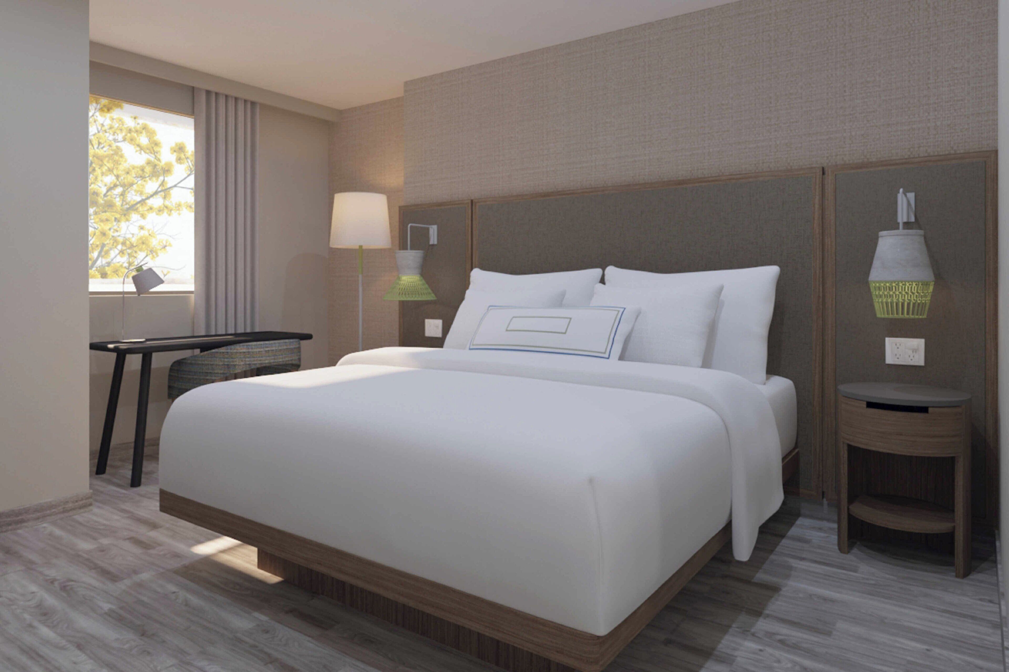 Quarto de hotel moderno com uma cama grande, uma escrivaninha, uma luminária e vista para árvores pela janela.