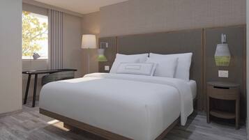 Quarto de hotel moderno com uma cama grande, uma escrivaninha, uma luminária e vista para árvores pela janela.