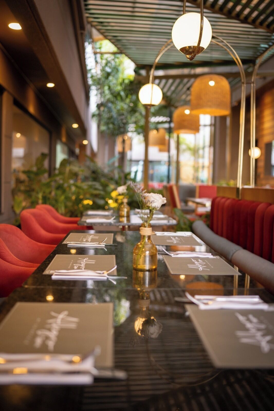 A restaurant with a long table set for dining, red upholstered chairs, and a bottle of wine on the table.