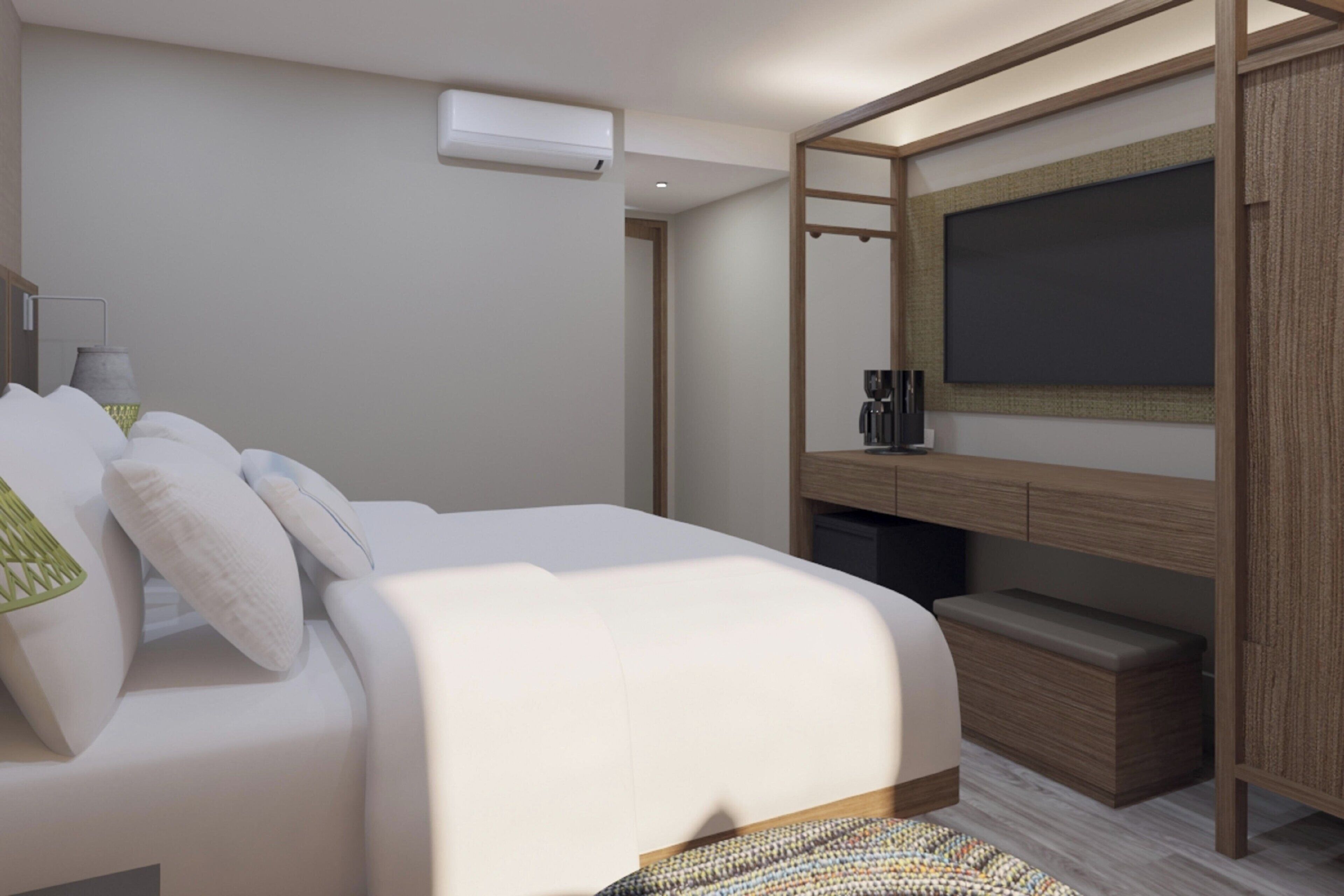 A modern hotel room with a large bed, a flat-screen TV mounted on the wall, a wooden bedside table, and a built-in bench.