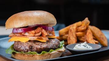 A burger with bacon, cheese, and lettuce on a bun, served with fries and a side of sauce.