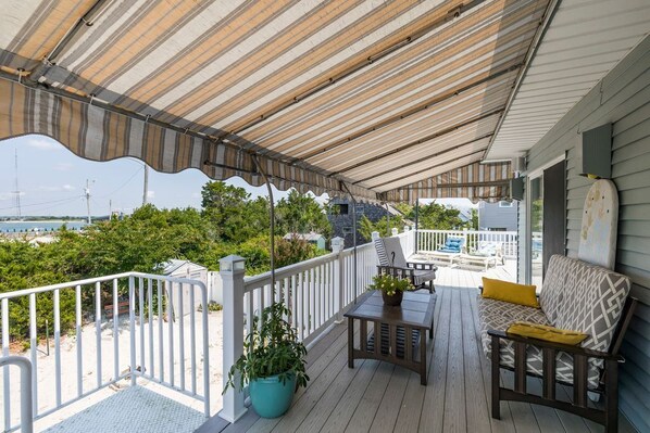 Eine überdachte Terrasse im Freien mit weißer Geländer, einem Holztisch, einer Couch und einem Topf mit Pflanze.