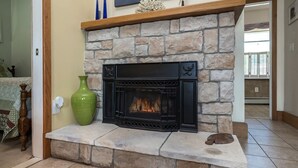 Une cheminée en pierre avec un manteau noir, un vase vert et une sculpture de poisson sur le foyer.