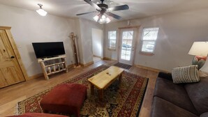 A living room with a television on a wooden stand, a ceiling fan, a wooden door, and a patterned rug.