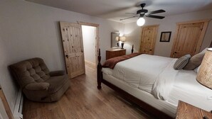 A bedroom with a bed, a chair, wooden wardrobes, a ceiling fan, and a nightstand with a lamp.