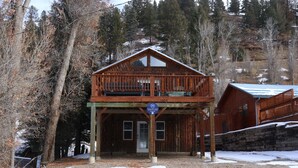 A wooden cabin with a balcony, a sign indicating it is a vacation rental, and a view of the surrounding forest.